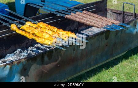 Mittelöstliche Kabobs auf einem Grill. Es gibt sowohl gelbe Hühnerkabobs als auch braune Rinderkabobs. Sie sind mit flachen Metallmessern über einem langen Spieß Stockfoto