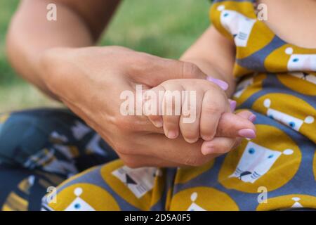 Eine Babyhand hält die Hand der Mutter. Glückliches Familien- und Babyschutzkonzept Stockfoto