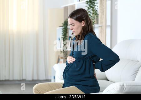 Schwangere Frau mit Rückenschmerzen beschwert sitzen auf einem Sofa Im Wohnzimmer zu Hause Stockfoto