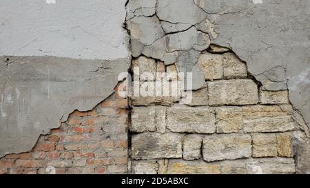 Alte, verwitterte, beschädigte Wand eines baufälligen Gebäudes. Grunge texturierter Hintergrund aus Mauerwerk und Kalkstein Mauerwerk mit rauhen gesprungenen Zement bedeckt Stockfoto