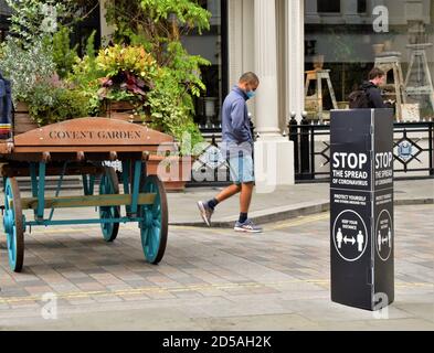 Ein Mann mit einer schützenden Gesichtsmaske geht an einem Stop the Ausbreitung von Coronavirus sozialen distanzierenden Straßenschild in Covent Garden, London vorbei Stockfoto