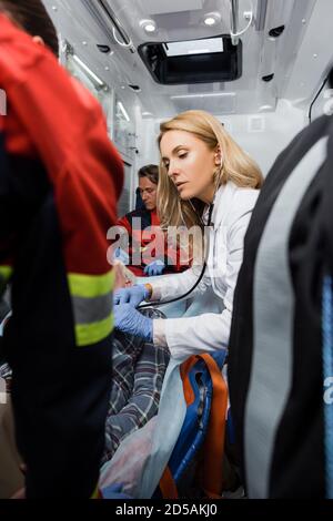 Selektiver Fokus des Arztes, der den Patienten mit Stethoskop in der Nähe von Sanitätern untersucht Im Krankenwagen Stockfoto