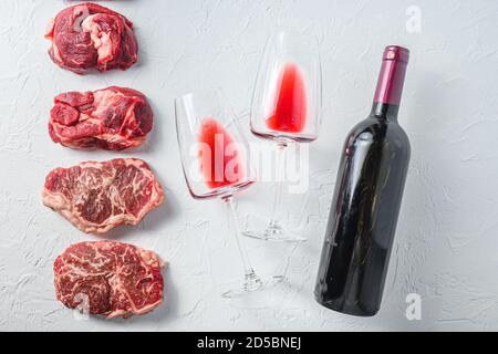 Rohes Set von alternativen Beef Cuts Chuck Augenrolle, Top Blade, Rumpsteak mit Rotwein in Glas und Flasche. Bio-Fleisch. Weißer strukturierter Hintergrund.Oberteil Stockfoto