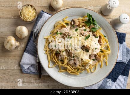 Cremige Fettuccine alfredo mit Pilzen und zerfetztem Parmesan auf einem Teller. Overhead-Ansicht Stockfoto