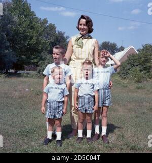 1960er Jahre, historisch, Sommerzeit und im Freien stehend in einem grasbewachsenen Feld für ein Familienbild, eine stolze Mutter mit ihren vier jungen Söhnen, alle mit blonden Haaren und in passenden hellblauen T-Shirts, karierte Shorts und weiße Socken. In dieser Zeit war es üblich, dass eine Mutter ihre Jungen in die gleichen Outfits kleiden oder auskleiden sollte. Stockfoto