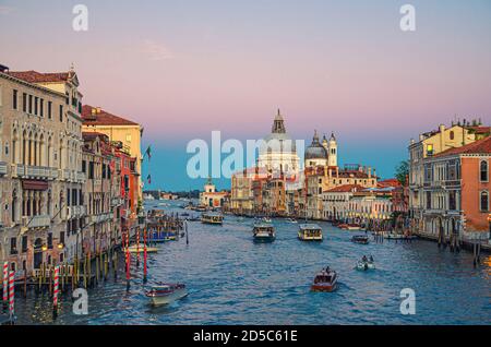 Venedig Stadtbild mit Grand Canal Wasserstraße. Gebäude mit Abendlicht entlang des Canale Grande. Die römisch-katholische Kirche Santa Maria della Salute befindet sich in der Dämmerung auf der Punta della Dogana. Region Venetien, Italien. Stockfoto