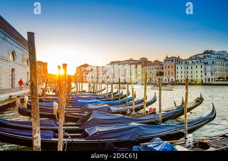 Gondeln, die an der Anlegestelle des Canale Grande in Venedig festgemacht sind. Barocke Gebäude entlang des Canal Grande im Hintergrund. Blick gegen die Sonne. Erstaunliche Venedig Stadtlandschaft bei Sonnenuntergang. Region Venetien, Italien Stockfoto