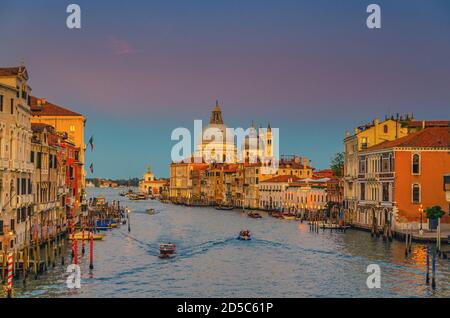 Venedig Stadtbild mit Grand Canal Wasserstraße. Gebäude mit Abendlicht entlang des Canale Grande. Die römisch-katholische Kirche Santa Maria della Salute befindet sich in der Dämmerung auf der Punta della Dogana. Region Venetien, Italien. Stockfoto