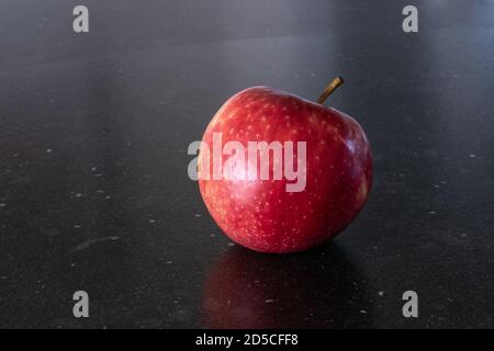 Ein Apfel am Tag hält den Arzt fern. Ein roter leckerer und glänzernder Apfel auf dunklem Hintergrund, Küchentischplatte. Gesunde Snacks und gesunde Ernährung Stockfoto