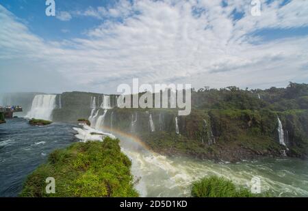 Landschaftlich schöner Blick über die Iguazzu Wasserfälle in brasilien. Wenn die Sonne durch die Wolkendecke bricht, bilden sich Regenbögen im Spray. Stockfoto