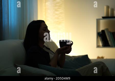 Profil Silhouette einer Frau trinken Kaffee zu Hause in Die dunkle Nacht auf einer Couch sitzend