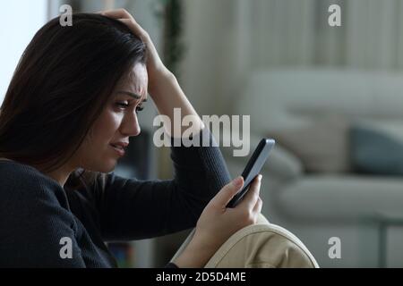 Traurige Frau, die schlechte Nachrichten auf dem Handy liest und sich beschwert Zuhause in der Nacht Stockfoto