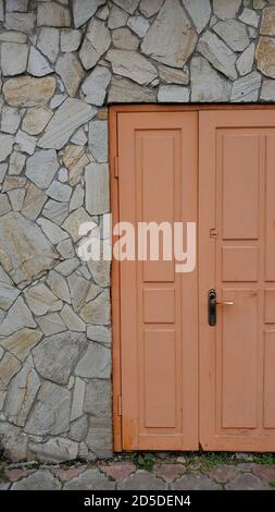 Retro gerahmte Holztür in helloranger Farbe gestrichen. Eingang des alten Gebäudes mit Backsteinmauer mit rauen natürlichen Felsen Stockfoto