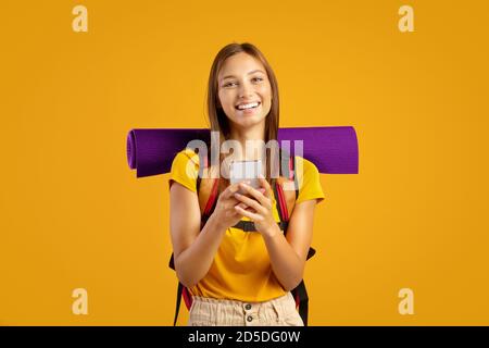 Glückliche junge Frau mit Rucksack hält Handy Stockfoto