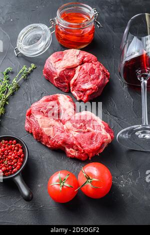 Bio-Chuck Eye Roll Steak Schnitte, mit Rotweinglas, Rosmarin, würziges Chili-Öl auf schwarzem texturierten Hintergrund Seitenansicht Stockfoto