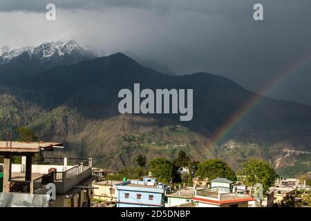 Ein Regenbogen über einem schneebedeckten Himalaya-Berg über den Dächern des Dorfes Munsyari in Uttarakhand. Stockfoto