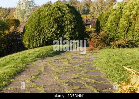 Park mit grünem Rasen, Bäume getrimmt Sträucher und Natursteinpfad im Herbst. Modernes Landschaftsdesign. Stockfoto