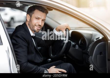 Glücklicher junger Unternehmer, der im Auto sitzt und zum Flughafen fährt Stockfoto