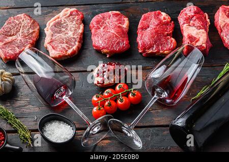 Set aus verschiedenen rohen Rindfleisch Steaks mit Gewürzen und Rotwein in Flasche und Glas auf alten hölzernen dunklen Bretter Seitenansicht. Stockfoto