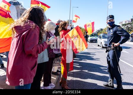 Menschen, die vor einem Polizeibeamten Flaggen schwenken, während sie an einem Protest gegen die Behandlung der COVID-19-Krise durch die spanische Regierung teilnehmen. Stockfoto