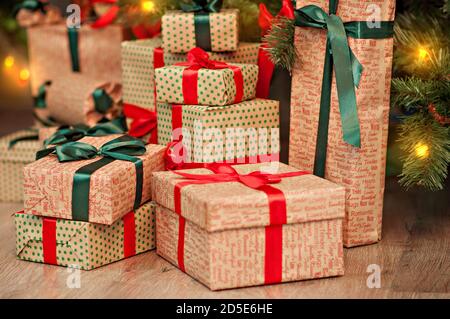 Ein hoher Berg von Geschenken unter einem Weihnachtsbaum in Lichterketten in rot-grünem Geschenkpapier mit Schleifen. Neujahrskarte. Weihnachtsmann Stockfoto