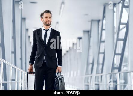 Reicher Unternehmer in schwarzem Anzug geht durch den modernen Flughafen Stockfoto