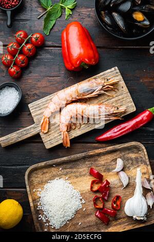 Traditionelle Paella valenciana Rohzutaten mit Garnelen, Muscheln, Reis und Tintenfisch auf dunklem rustikalem Holzhintergrund, flaches Lay Stockfoto