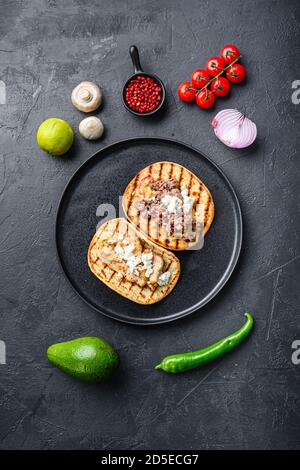 Traditionelle mexikanische Tortilla mit Huhn und Rindfleisch mit Zutaten eine Seite auf schwarzem Teller über schwarz texturierten Hintergrund Draufsicht. Stockfoto