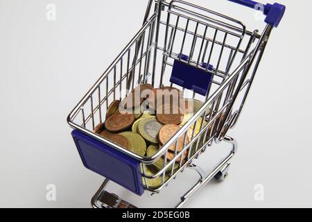 Blick auf isolierte Warenkorb-Modell mit kleinen losen Wechselmünzen, weißer leerer Hintergrund - Kaufkraftkonzept (Fokus auf Geldstapel) Stockfoto