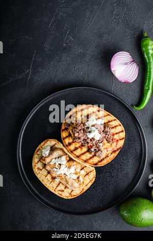 Mexikanische Tacos mit Gemüse und Beeaf und Hühnerfleisch auf schwarzem runden Teller über texturiertem schwarzen Hintergrund, Draufsicht, selektiver Fokus mit Platz für Stockfoto