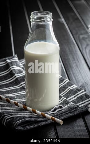 Frische Milch in Glasflasche auf Küchenserviette auf schwarzem Tisch. Stockfoto