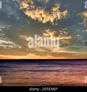 Wunderschöner Sonnenuntergang über ruhigem Wasser mit dramatischen Wolken und lebhaften Farben in der Dämmerung. Bretagne. Frankreich Stockfoto