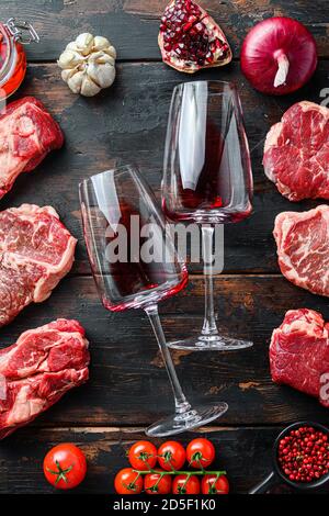 Fleischbeef Steaks Rahmenkonzept, mit verschiedenen Steaks und zwei Weingläsern im Rahmen auf dunklem alten Holztisch Draufsicht. Stockfoto