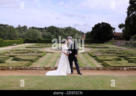 Braut und Bräutigam küssen sich am Hochzeitstag vor den formellen Gärten am Penshurst Place. Braut & Bräutigam küssen. Bräutigam trägt graue Zylinderhut und Schwanz. Stockfoto