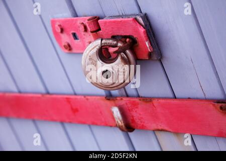 Silbernes Vorhängeschloss an der blau-violetten Tür mit roter Sicherheitsstange. Doppeltüren mit Vorhängeschloss. Stockfoto