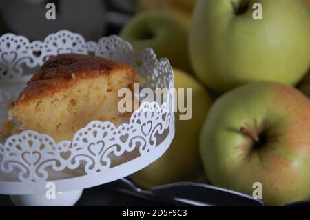 Eine Scheibe Apfelkuchen Nahaufnahme auf weißem Kuchen Stand und einige gelbe Äpfel im Hintergrund. Kochen zu Hause. Stockfoto