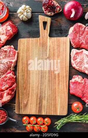 Fleischbeef Steaks Rahmenkonzept, mit verschiedenen Steaks und leerem Schneidebrett in Rahmen auf dunklem alten Holztisch Draufsicht. Stockfoto