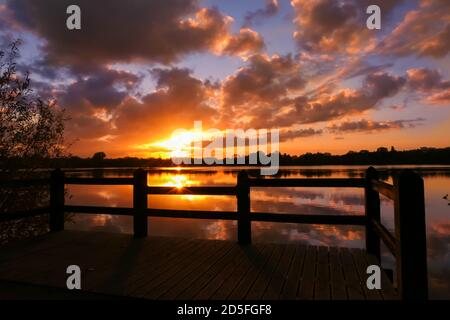 Erstaunlicher Sonnenaufgang in ländlicher Umgebung. Symmetrie des Himmels in einem See bei Sonnenuntergang. Wolken spiegeln sich auf dem Wasser. Holzponton im Vordergrund. Stockfoto