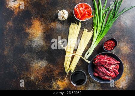 Rohzutaten zum Rühren Chinesische Nudeln mit Gemüse und Rindfleisch in schwarzer Schüssel anbraten. Auf alten rustikalen Tisch. Mit Platz für Text. Stockfoto