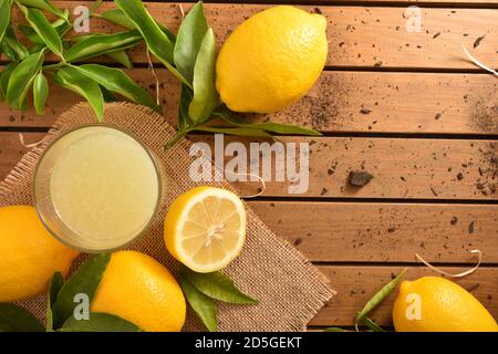 Frisch gepresster Saft auf einem Holztisch auf einem Sackleinen voller Zitronen. Draufsicht. Horizontale Zusammensetzung. Stockfoto