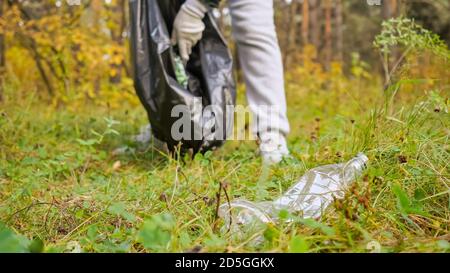 Junge Frau sammelt Müll in einem schwarzen Paket im Wald. Stockfoto