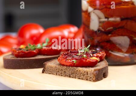 Hausgemachte sonnengetrocknete Tomaten mit Olivenöl in einem Glas. Sandwich mit schwarzem Brot und sonnengetrockneten Tomaten Stockfoto