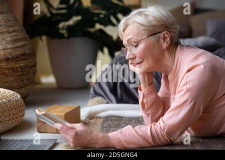 Ältere Frau mit Brille, die zu Hause ein Buch liest. Stockfoto