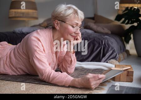 Ältere Frau mit Brille, die zu Hause ein Buch liest. Stockfoto