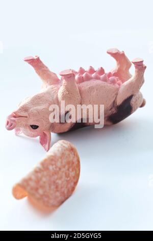 Miniatur-Kunststoff-Schwein mit einem Stück Wurst erschossen Weißer Hintergrund Stockfoto