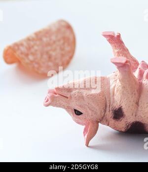 Miniatur-Kunststoff-Schwein mit einem Stück Wurst erschossen Weißer Hintergrund Stockfoto