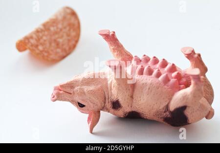 Miniatur-Kunststoff-Schwein mit einem Stück Wurst erschossen Weißer Hintergrund Stockfoto