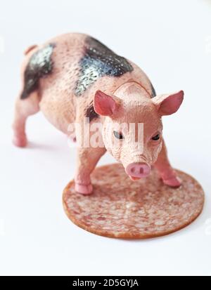 Miniatur-Kunststoff-Schwein mit einem Stück Wurst erschossen Weißer Hintergrund Stockfoto