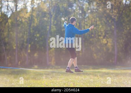 Mann Wandern, Springen und Balancieren am Seil im Park Sport eine Drahtseilbahn oder Slackline im Freien in einem Stadtpark im Sommer Slacklining, Balance, Training Stockfoto