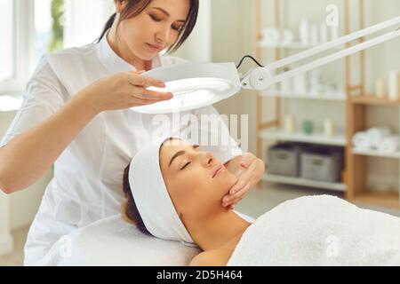 Frau Kosmetologe Blick auf heitere junge Frauen Gesicht anc Überprüfung Hautzustand Stockfoto